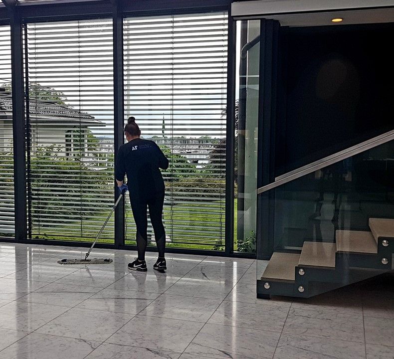Renholder vasker gulvet ved en glassvegg.