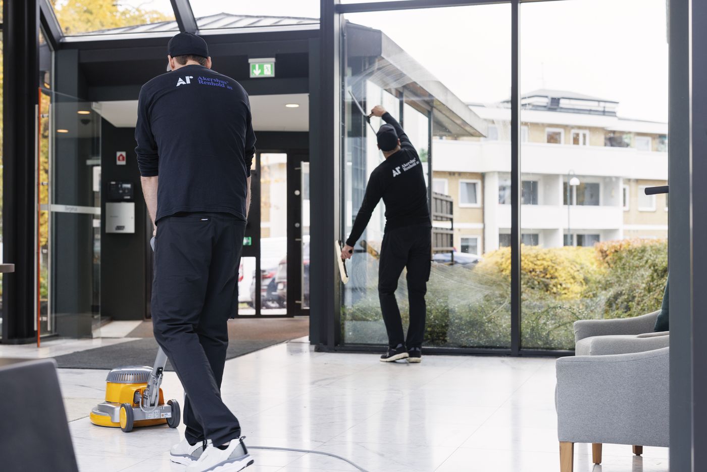 Renholdere vasker glassvegger og gulv i en resepsjon.