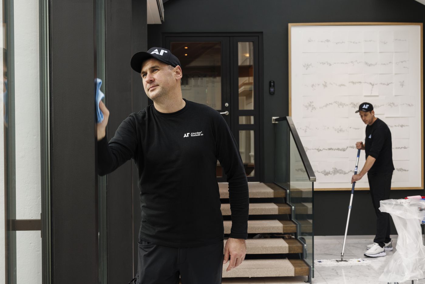 Renholder i Akershus Renhold-uniform tørker av en glassvegg ved trappen.